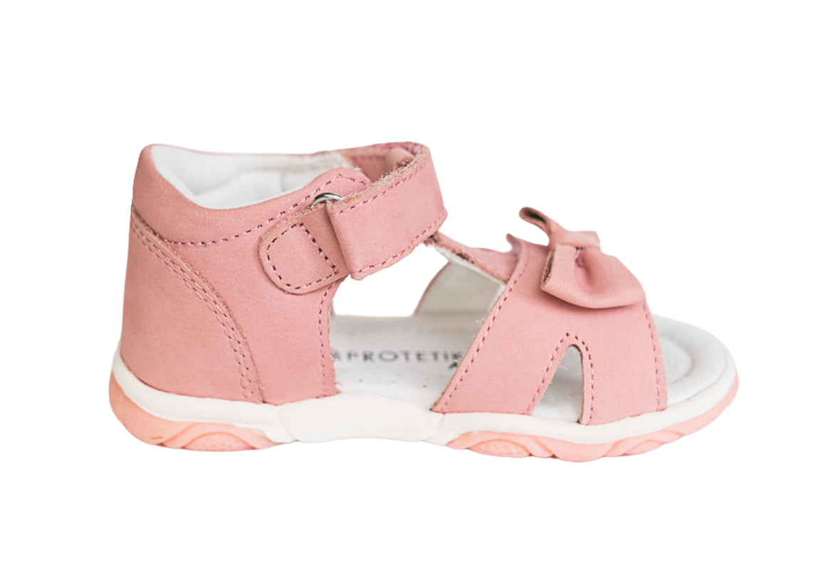 A pink toddler girl Protetika sandal with an arch support, a hook-and-loop strap closure and a decorative bow detail in the front.